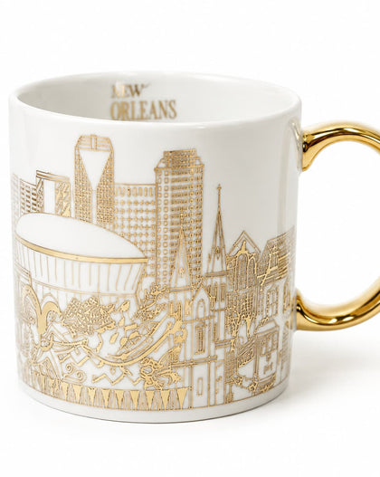A white ceramic coffee mug featuring a gold line-art illustration of the New Orleans skyline and the word 'NEW ORLEANS' printed inside the rim, with a polished gold handle.