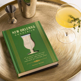 Book titled 'New Orleans Cocktails' on a gold tray with a cocktail glass and bar tools.