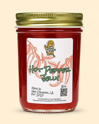 A jar of Fancy Farming Kitchen Hot Pepper Jelly with a gold metal lid and a white label featuring red pepper illustrations, set against a solid light beige background.