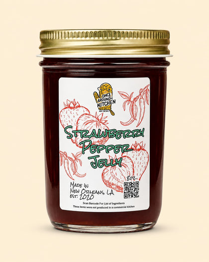 A glass jar of Strawberry Pepper Jelly with a gold metal lid and a white label featuring red strawberry illustrations and green text, set against a solid beige background.