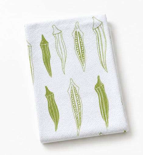 A folded white kitchen towel featuring a green line-art pattern of okra pods, photographed on a clean white background.
