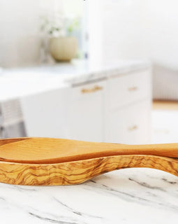 Hand-carved olive wood spoon rest with curved bowl and rich natural grain on a white background.