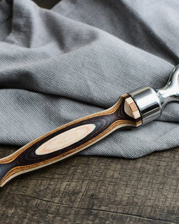 Pakka wood handle bottle opener with stainless steel head resting on a wooden surface