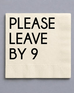 An off-white paper napkin with black printed text reading 'PLEASE LEAVE BY 9' on a solid gray background.