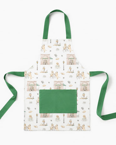 A white apron with a green neck strap and waist ties, featuring a repeating pattern of vintage illustrations of people sitting at tables and a large solid green front pocket.