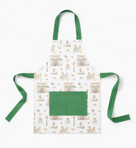 A white apron with a green neck strap and waist ties, featuring a repeating pattern of vintage illustrations of people sitting at tables and a large solid green front pocket.