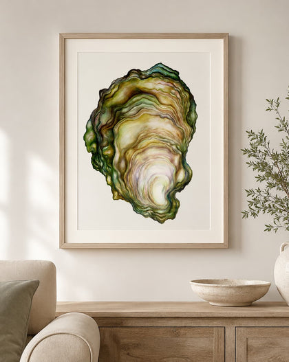 A framed art print featuring a detailed watercolor illustration of an oyster shell, styled in a light wood frame on a neutral wall above a wooden console table with a vase and bowl.