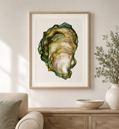 A framed art print featuring a detailed watercolor illustration of an oyster shell, styled in a light wood frame on a neutral wall above a wooden console table with a vase and bowl.
