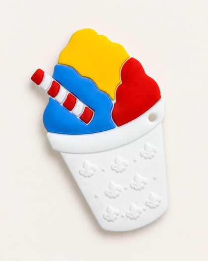 A silicone baby teether shaped like a snowball featuring yellow, blue, and red scoops with a red-and-white striped straw, set against a light beige background.