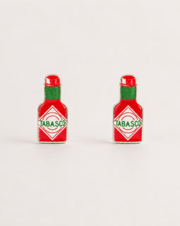 Two small Tabasco bottle-shaped earrings shown on a plain light background. Each piece is red with a green neck and a white diamond label featuring the green Tabasco brand name.