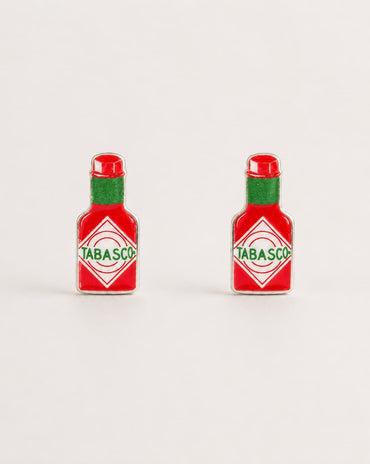 Two small Tabasco bottle-shaped earrings shown on a plain light background. Each piece is red with a green neck and a white diamond label featuring the green Tabasco brand name.