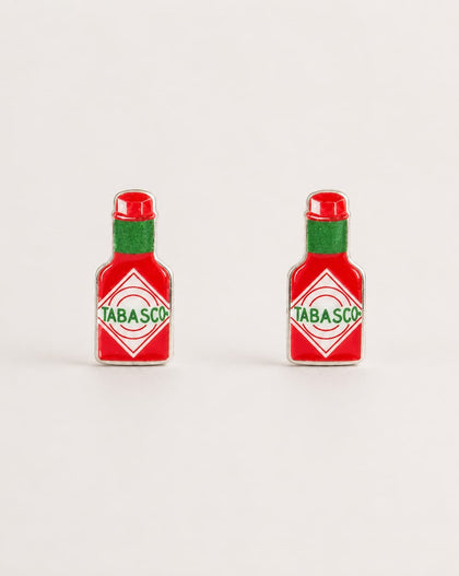 Two small Tabasco bottle-shaped earrings shown on a plain light background. Each piece is red with a green neck and a white diamond label featuring the green Tabasco brand name.