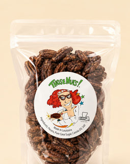 A clear stand-up pouch filled with roasted pecans, featuring a round white label with the brand name 'Those Muts!' and a cartoon illustration, set against a solid light beige background.