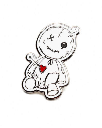 A small enamel pin shaped like a stitched voodoo doll, featuring a white face and body outline with black stitched details, a red heart on the chest, and a silver metal border, shown on a plain white background.