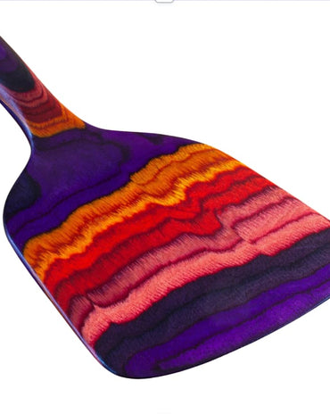 Colorful layered birch slotted spatula from the Waikiki Collection with vibrant purple, red, orange, and pink tones inspired by Hawaiian sunsets.