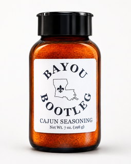 A 7 oz amber glass spice jar filled with orange Cajun seasoning, featuring a black screw cap and a white label with the brand name 'Bayou Bootleg'.