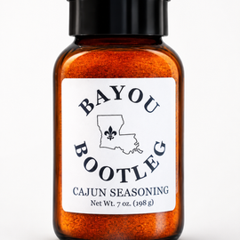 A 7 oz amber glass spice jar filled with orange Cajun seasoning, featuring a black screw cap and a white label with the brand name 'Bayou Bootleg'.