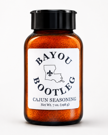 A 7 oz amber glass spice jar filled with orange Cajun seasoning, featuring a black screw cap and a white label with the brand name 'Bayou Bootleg'.
