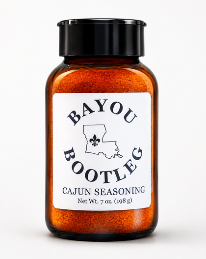 A 7 oz amber glass spice jar filled with orange Cajun seasoning, featuring a black screw cap and a white label with the brand name 'Bayou Bootleg'.