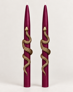 Set of two burgundy taper candles wrapped with gold snake accents on a neutral background.