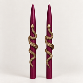 Set of two burgundy taper candles wrapped with gold snake accents on a neutral background.