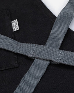 black canvas and leather chef apron with cross back straps, tool pockets, and metal hardware for cooking and grilling
