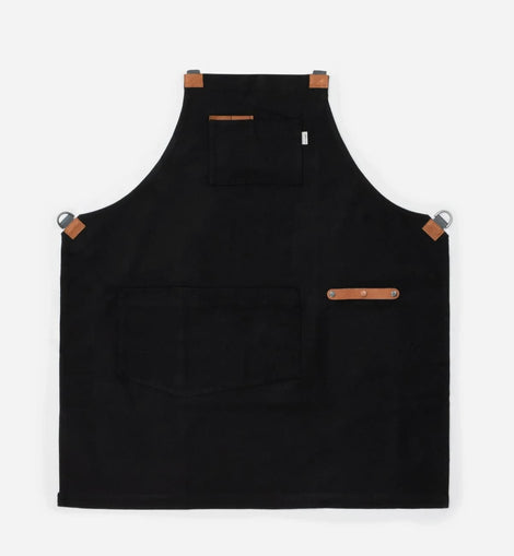 black canvas and leather chef apron with cross back straps, tool pockets, and metal hardware for cooking and grilling