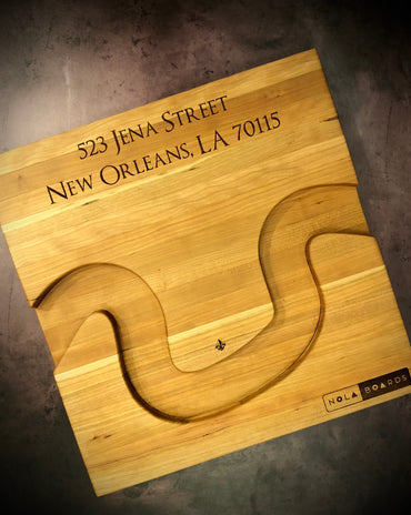 Handmade cherry Crescent City Board with curved edge holding crackers and olives, engraved with fleur de lis and address