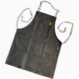 Dark denim workshop and grilling apron with reinforced utility pockets and adjustable straps on a neutral background