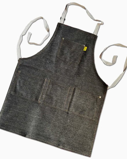 Dark denim workshop and grilling apron with reinforced utility pockets and adjustable straps on a neutral background
