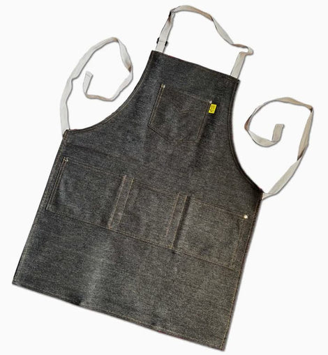 Dark denim workshop and grilling apron with reinforced utility pockets and adjustable straps on a neutral background