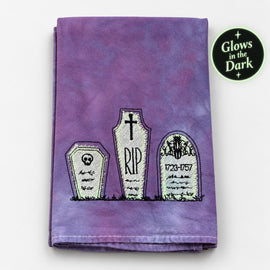 Hand-dyed purple tea towel with embroidered cemetery tombstones and glow-in-the-dark details.