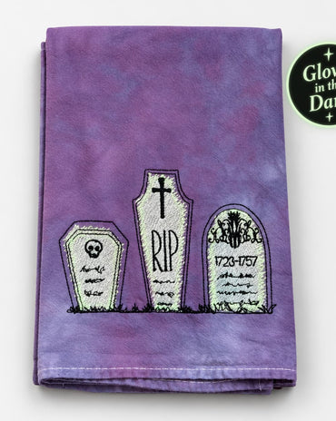 Hand-dyed purple tea towel with embroidered cemetery tombstones and glow-in-the-dark details.