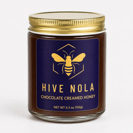 Jar of Hive Nola chocolate creamed honey with a gold lid on a white background