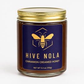 Jar of Hive Nola cinnamon creamed honey with a blue label and gold lid on a white background
