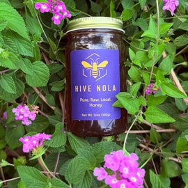 Jar of Hive Nola honey surrounded by green leaves and pink flowers