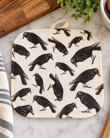 Cream pot holder with vintage-style black raven print displayed on a kitchen countertop.