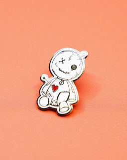 voodoo doll enamel pin with stitched details and red heart on orange background
