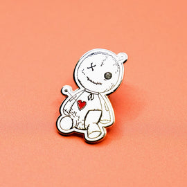 voodoo doll enamel pin with stitched details and red heart on orange background