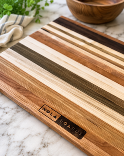 Wooden cutting board with striped pattern on a marble surface, featuring 'Nola Boards' branding.