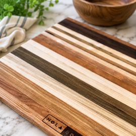 Wooden cutting board with striped pattern on a marble surface, featuring 'Nola Boards' branding.