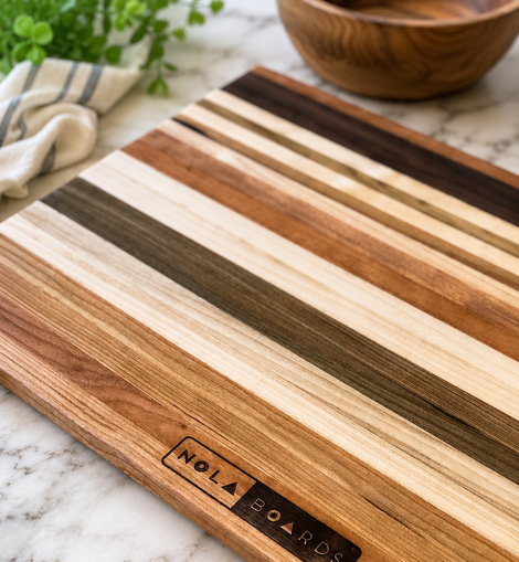 Wooden cutting board with striped pattern on a marble surface, featuring 'Nola Boards' branding.